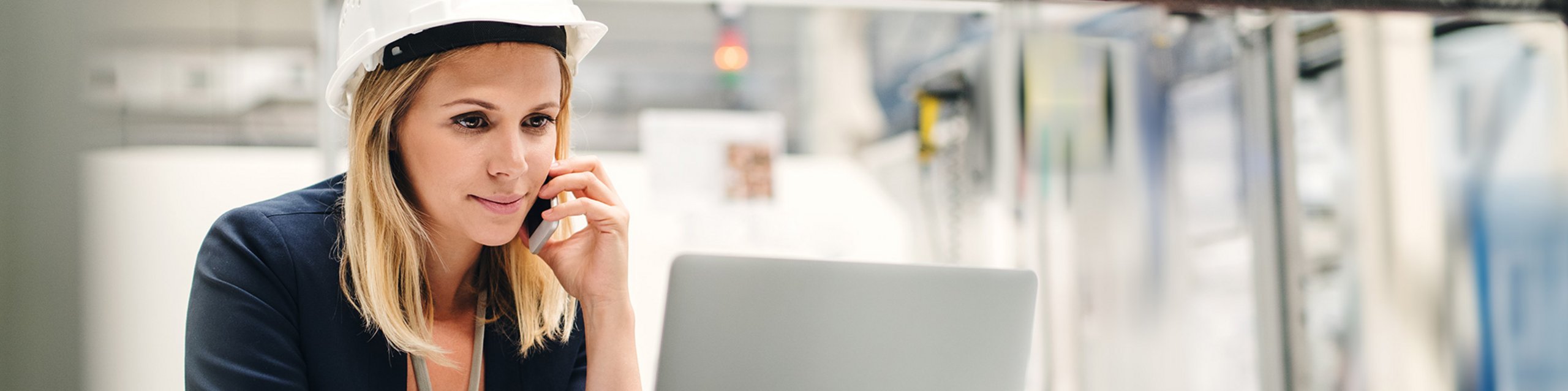 Frau mit Schutzhelm sitzt am Laptop und telefoniert